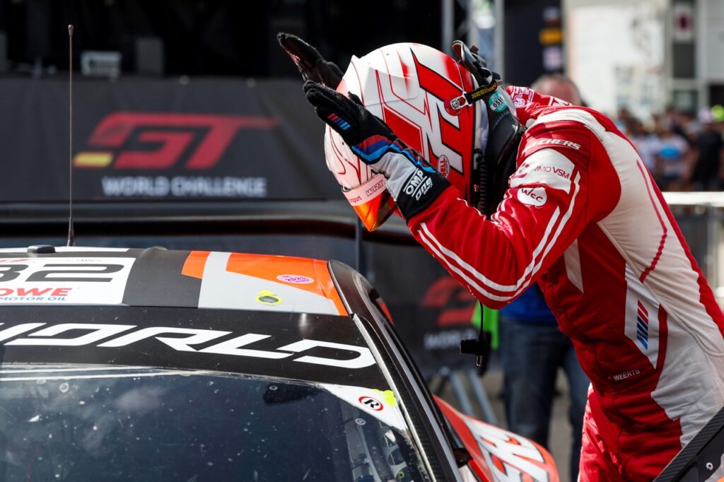 Charles Weerts of Team WRT in his helmet and race suit after a race leaning over the car 