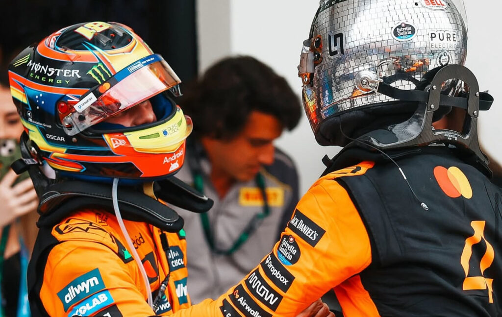 Miami GP victor Oscar Piastri in full race suit and helmet shaking hands post-race with Lando Norris.