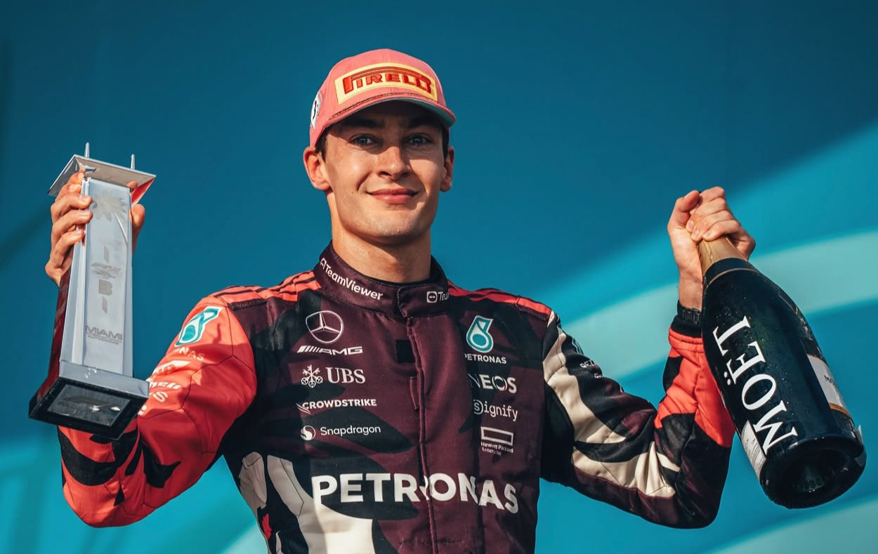 A jubilant George Russell on Miami GP podium with champagne and trophy.
